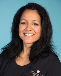 Dark haired woman wearing black scrubs smiling big