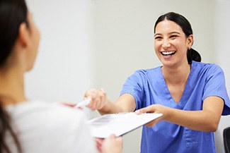 Smiling dental team member handing a clipboard to a patient