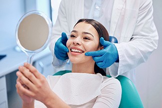 A young woman smiling and preparing to eat an apple with her fully restored smile thanks to CEREC dental crowns