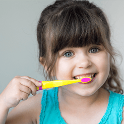 A little girl with brown hair brushing her teeth 