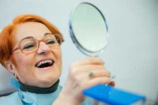 A woman admiring her dentures in a hand mirror