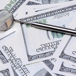 Money and dental mirror representing the cost of emergency dental care in Melbourne