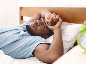 Man lying awake in bed with alarm clock nearby