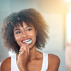 Woman smiling at reflection in mirror while brushing her teeth