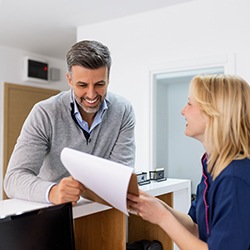 a front desk receptionist handing a piece of paper to a dental patient