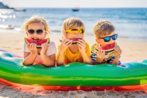 three kids eating watermelon on the beach to prevent dental emergencies 