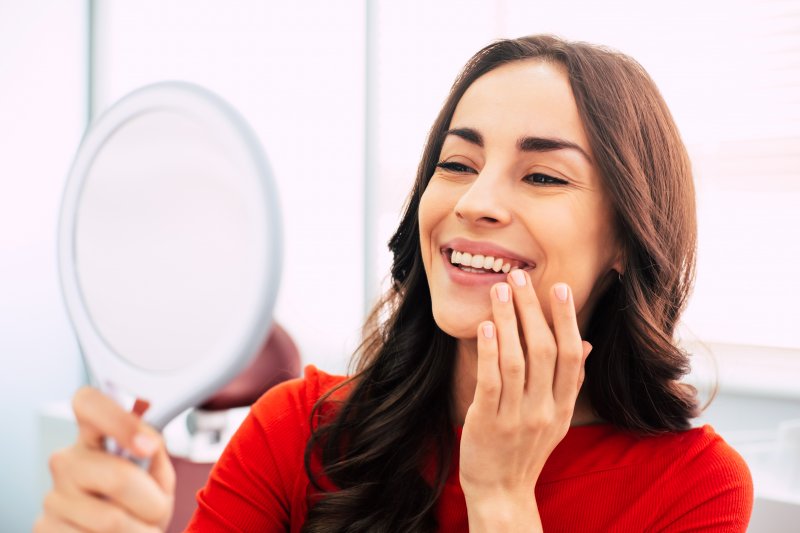 A woman smiling at her new dental veneers in a mirror