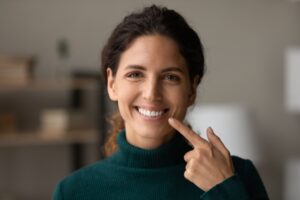 Woman with brown hair pointing to her smile