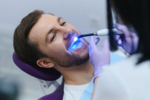 Dentist applying UV light to man's tooth-colored filling
